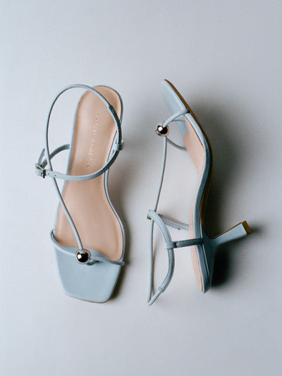 An overhead view of a pair of blue heeled strappy sandals one shoe on its side on a grey background.