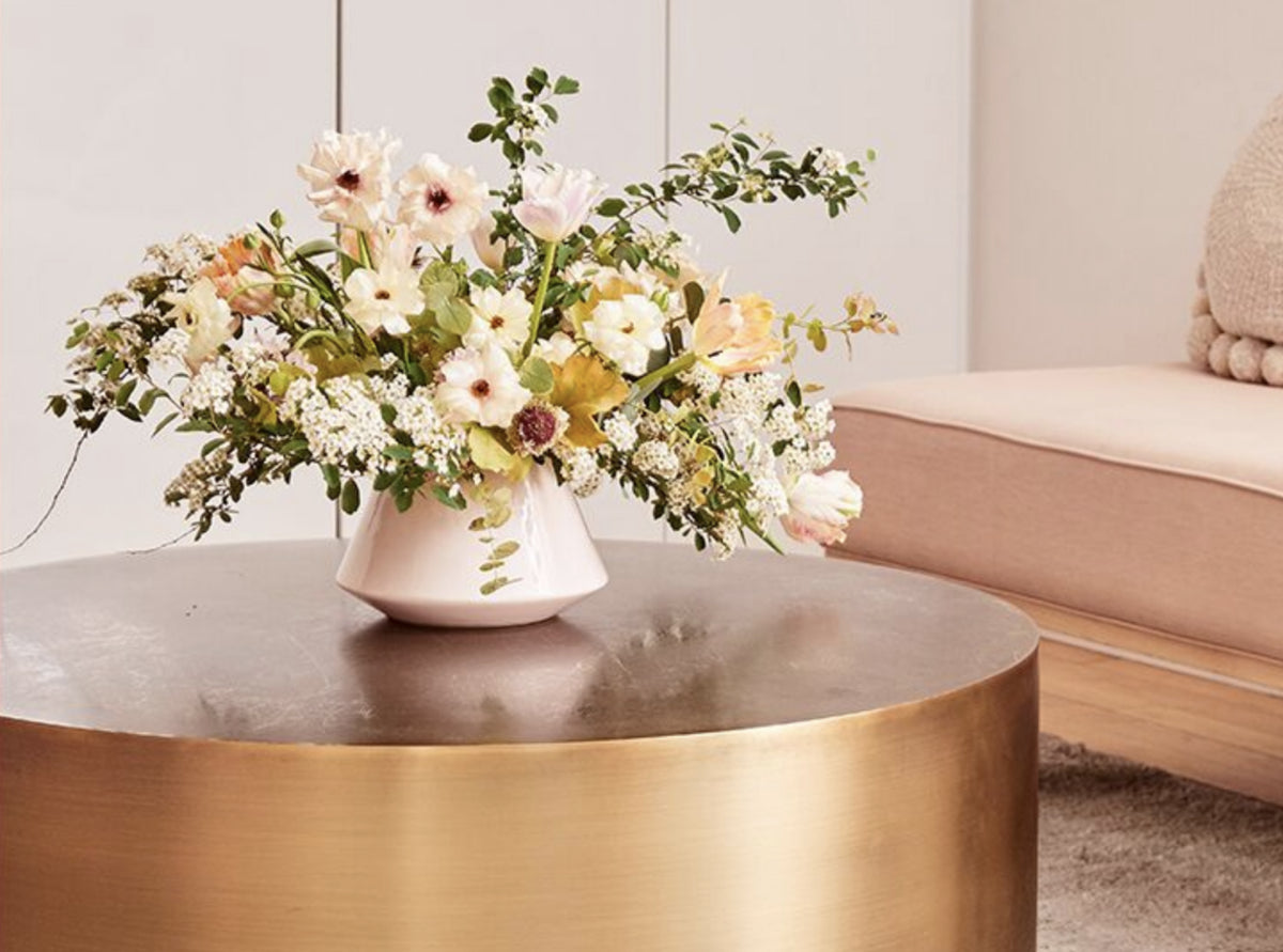 An arrangement of white and green flowers in a white vase on a gold table.