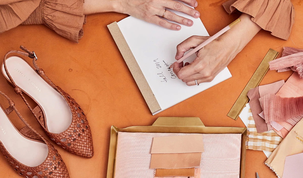 Someone writes on a white note pad with fabric swatches and shoes around them.