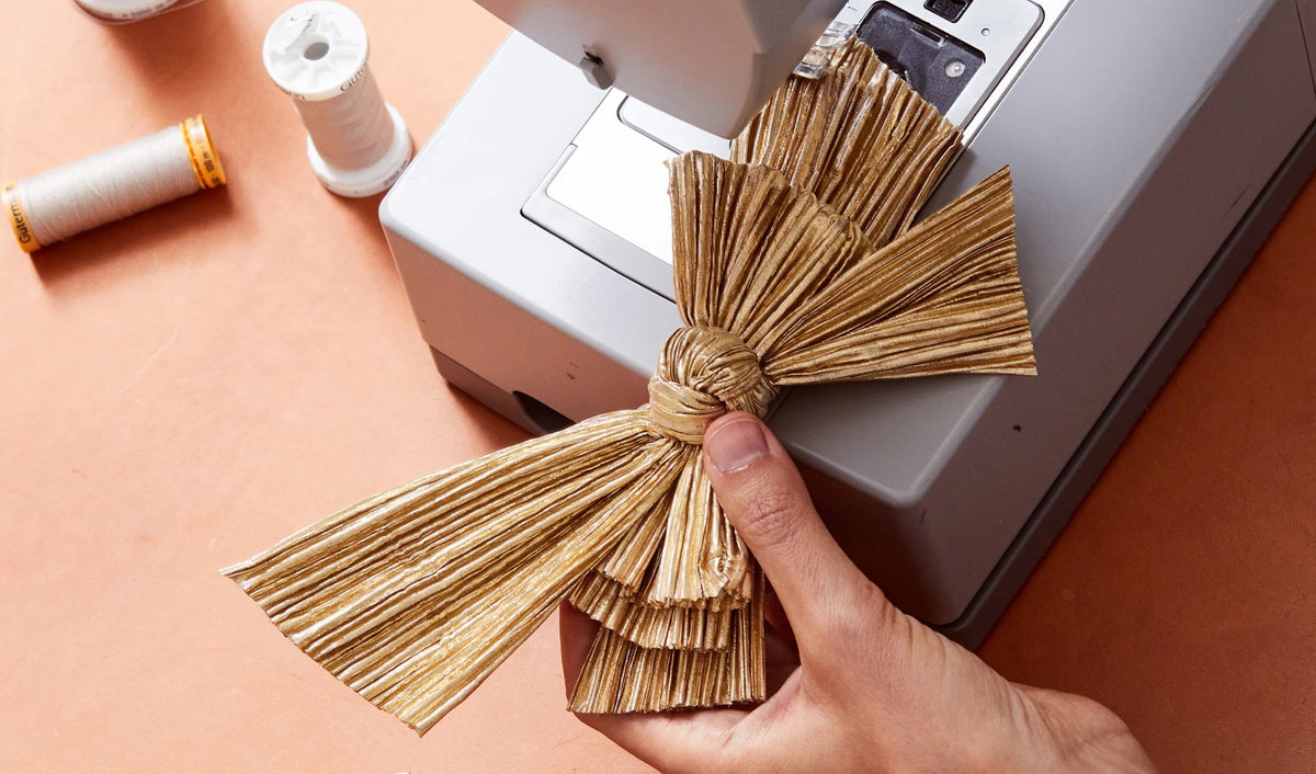 A gold pleated bow being finished on a sewing machine.