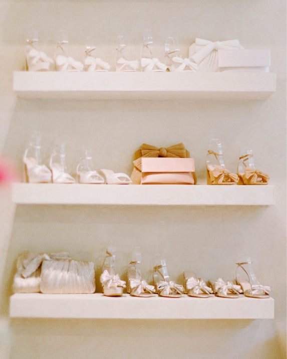 Three shelves at a store with assorted colors and styles of heeled sandals and clutches.