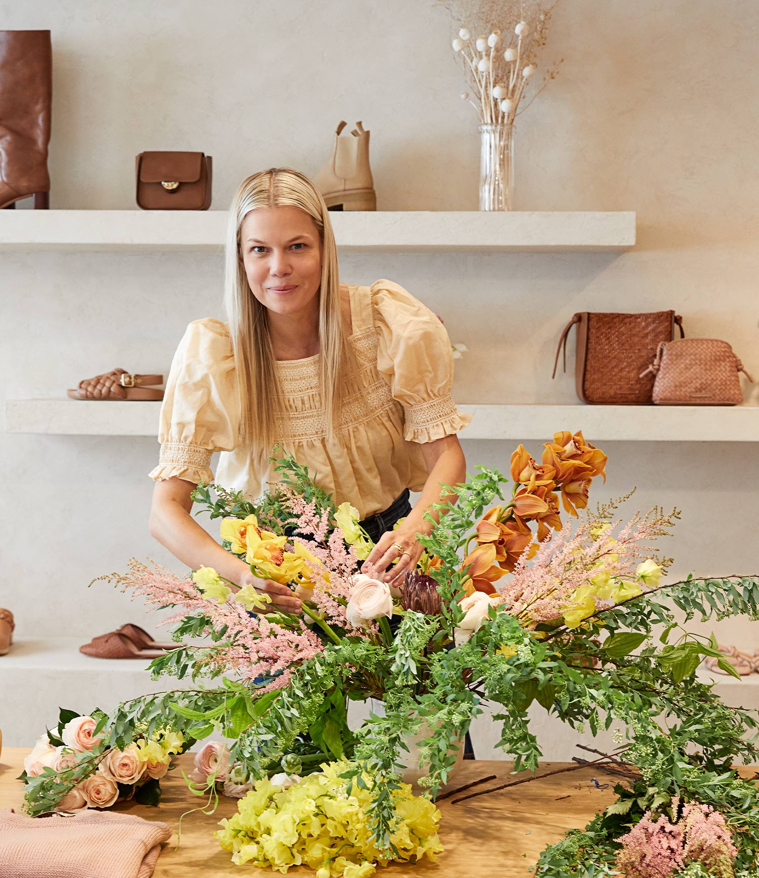 Jessie Randall arranges flowers in the center of our SoHo store with shelves behind her with assorted footwear and handbags.
