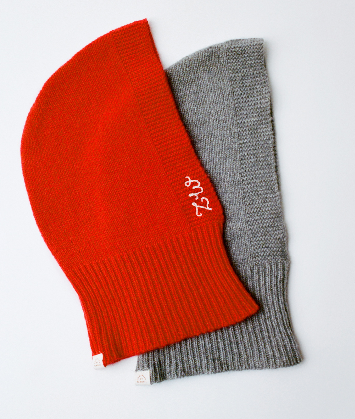 Two cashmere balaclavas one in red and one in grey on a grey background.