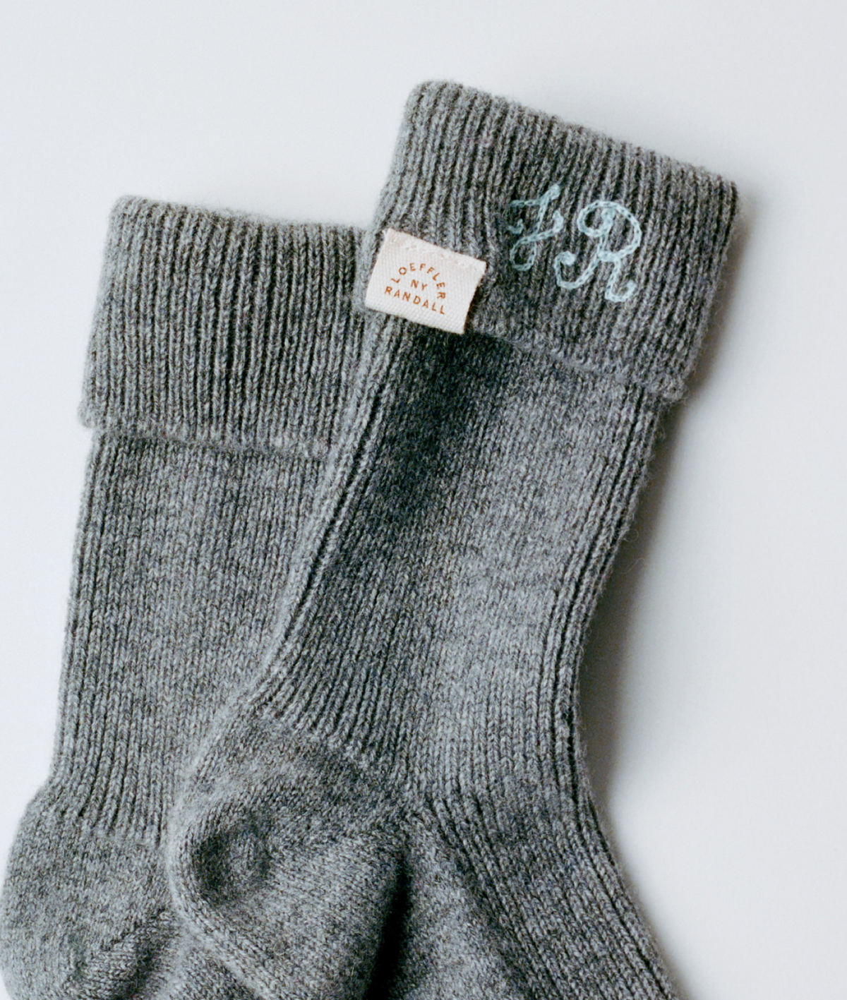 A pair of grey cashmere socks with a Loeffler Randall patch on a grey background.