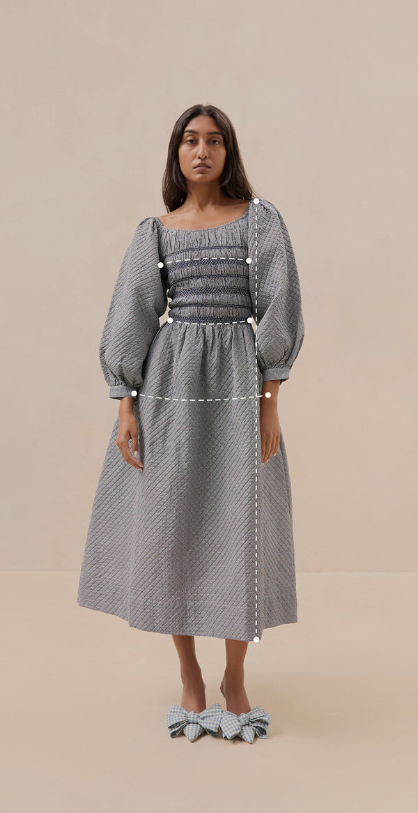A measurement guide of a model wearing a long sleeve dress. There are lines for measurement across her chest and waist and from the top of the shoulder to the bottom skirt hem.