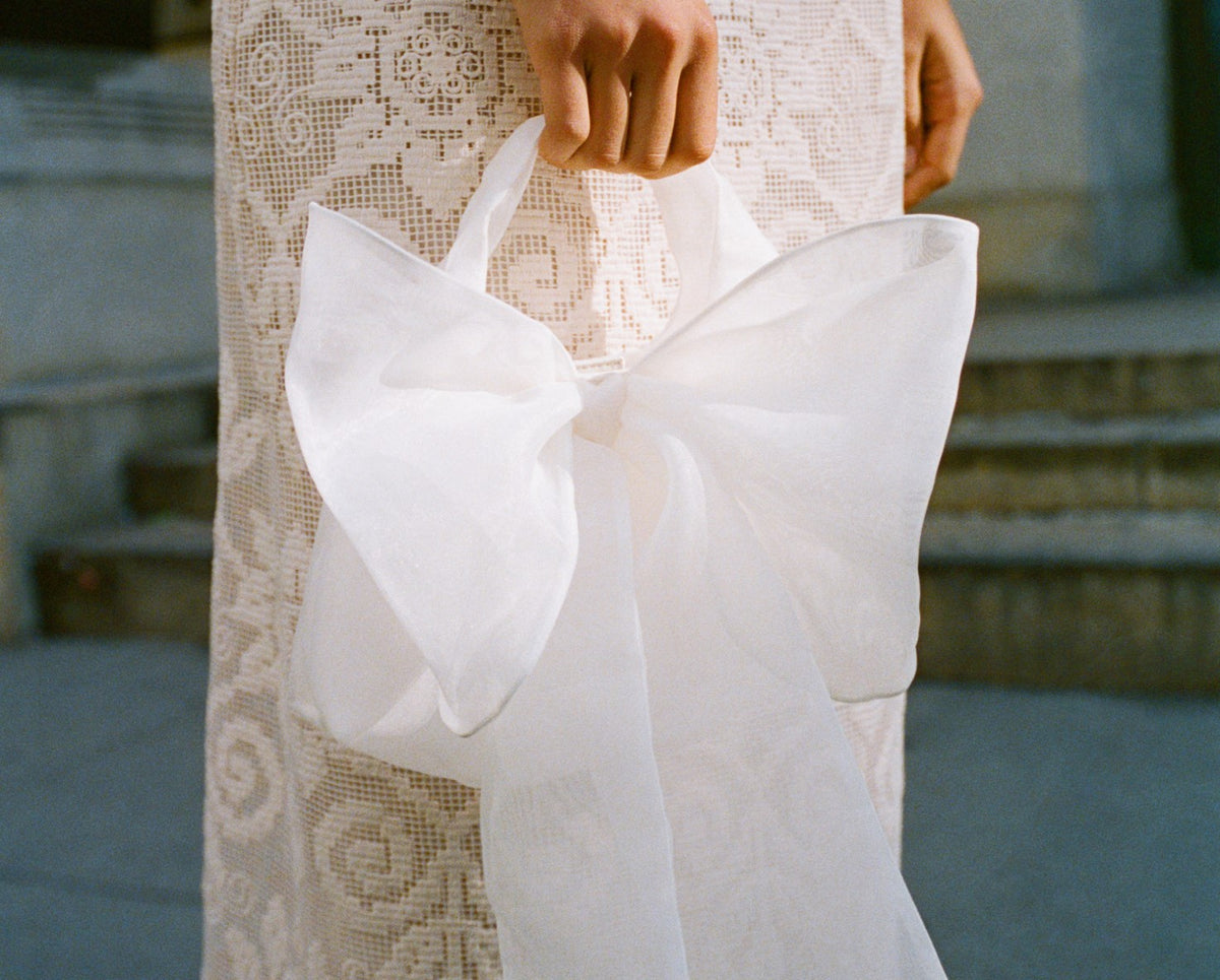 A model wearing a white lace dress holding a white bow clutch.