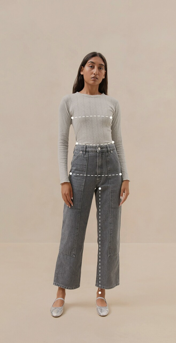 A model wears a grey long sleeve shirt tucked into grey jeans. There are measurement lines across her chest, waist, hips, and inseam.