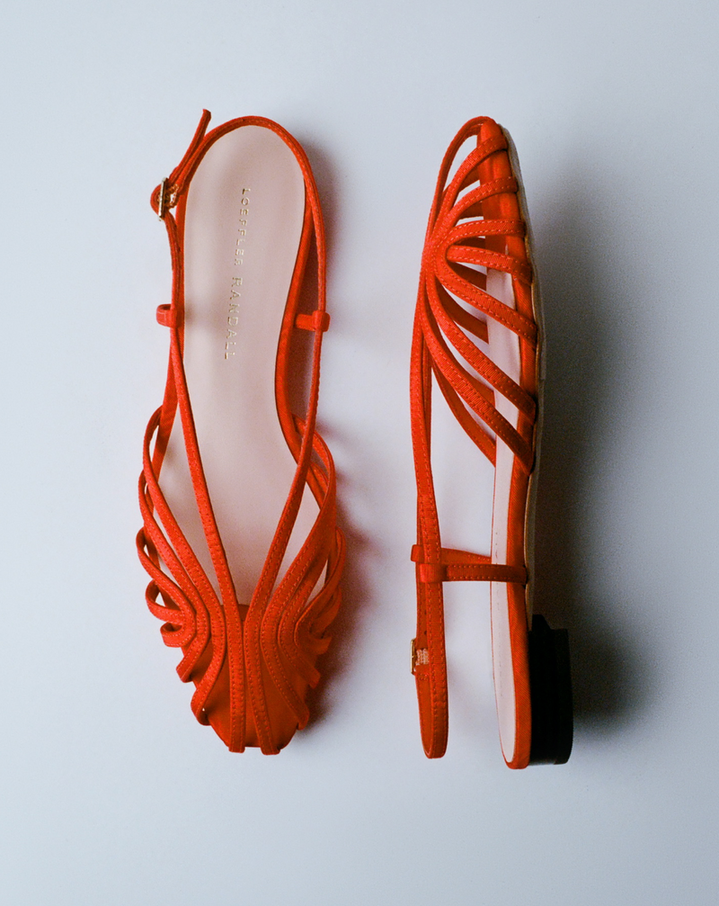 An overhead view of a pair of red lattice sandals with one on its side on a grey background.