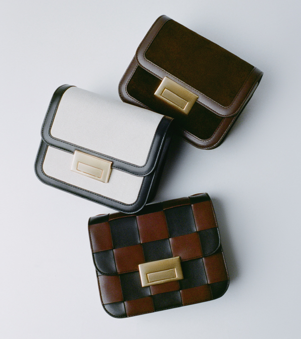 A cascade of three small handbags in different materials and colors with gold buckle accents on a light grey background.