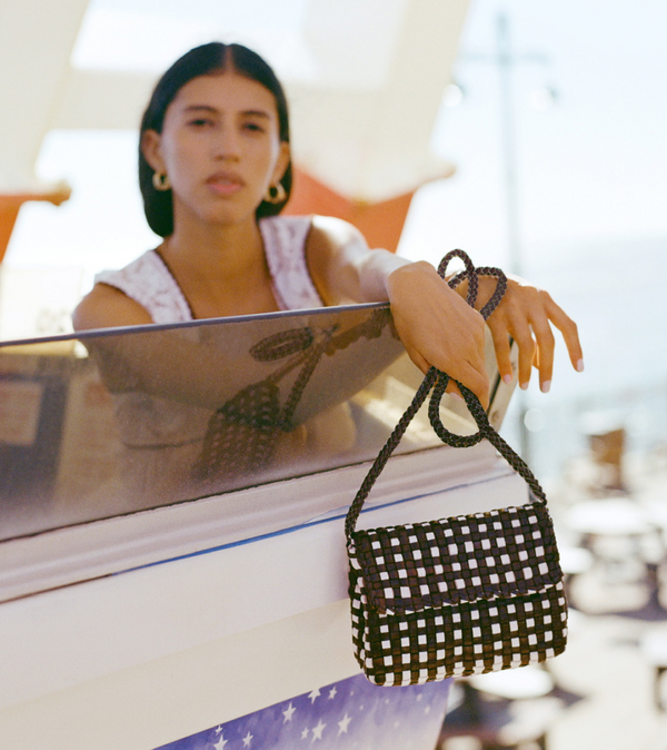 A model leans off of a glass ledge holding a brown and white checkered bag.