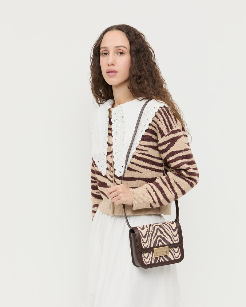 Desi Zebra Straw Crossbody in zebra woven cotton fabric with dark brown leather, Ken Shirt in white cotton, Bodhi Cardigan in zebra wool, and Delaney Skirt in white cotton.
