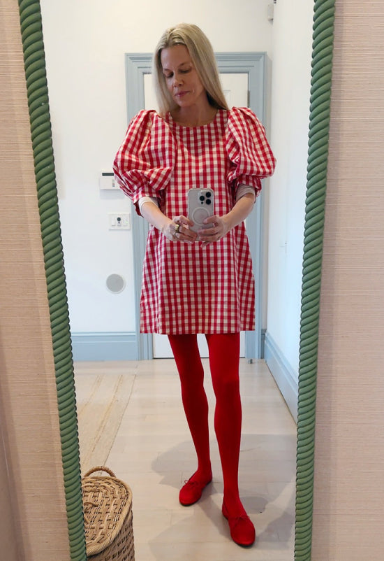 Jessie takes a mirror selfie wearing a red gingham dress, red tights, and red ballet flats.