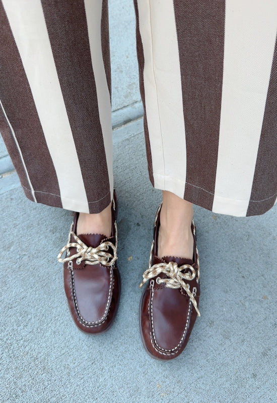 An overhead view of a model wearing brown boat shoes and striped pants standing on a sidewalk.