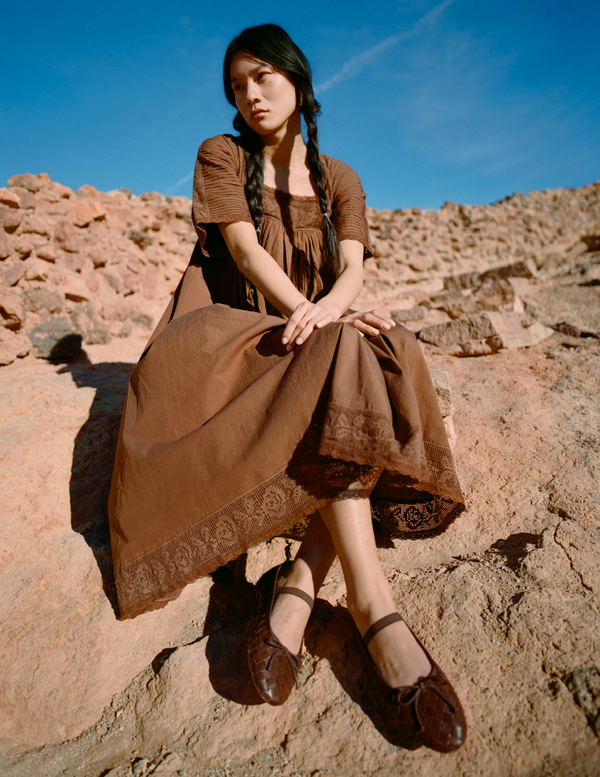 Woman in a brown dress sitting on rocky terrain with a blue sky in the background.