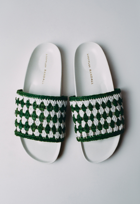 An overhead view of a slip on sandal with green and white crochet on a grey background.