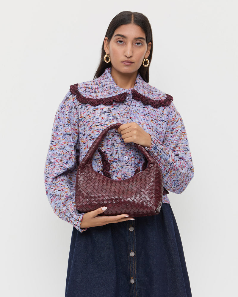 Mercer Maroon Woven Shoulder Bag in maroon woven leather, Lo Cardigan in marble maroon, and Ruthie Denim Skirt in dark blue.