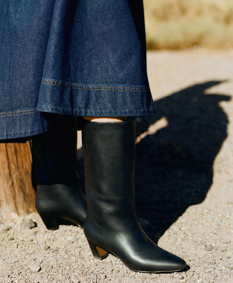 Someone wears a denim skirt and tall black leather boots.