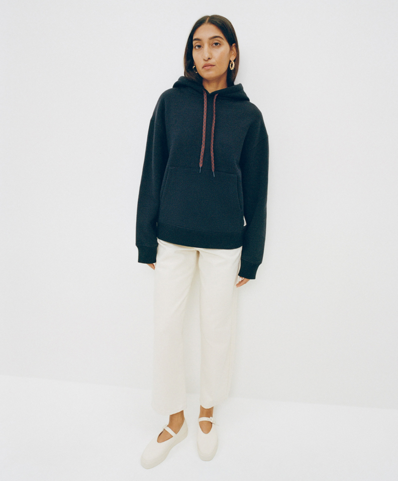 A model stands in front of a white background wearing a navy sweatshirt and white pants with white mary jane sneakers.