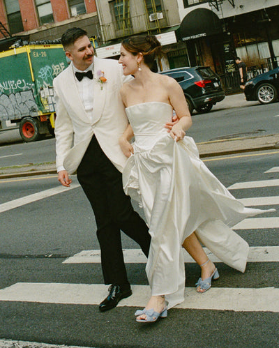 A bride and groom crossing a crosswalk in a city. The bride wears blue bow heels.
