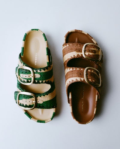 An overhead view of two double banded sandals with buckles, one in green and one in brown, on a grey background.