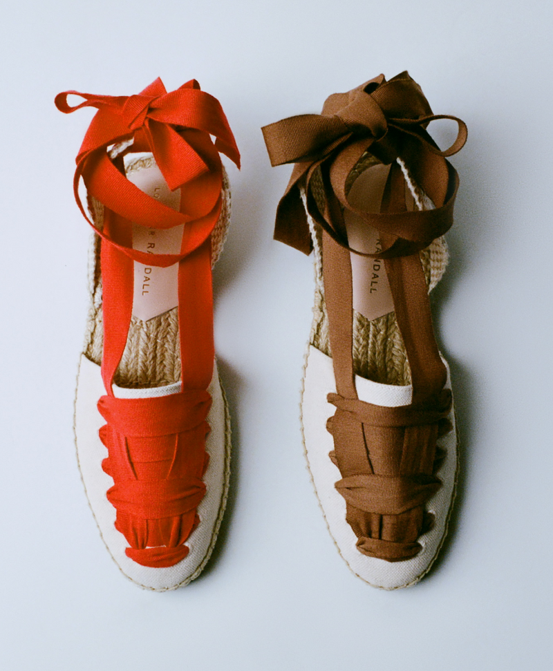 An overhead view of two lace up flat sandals, one in red and one in brown on a grey background.