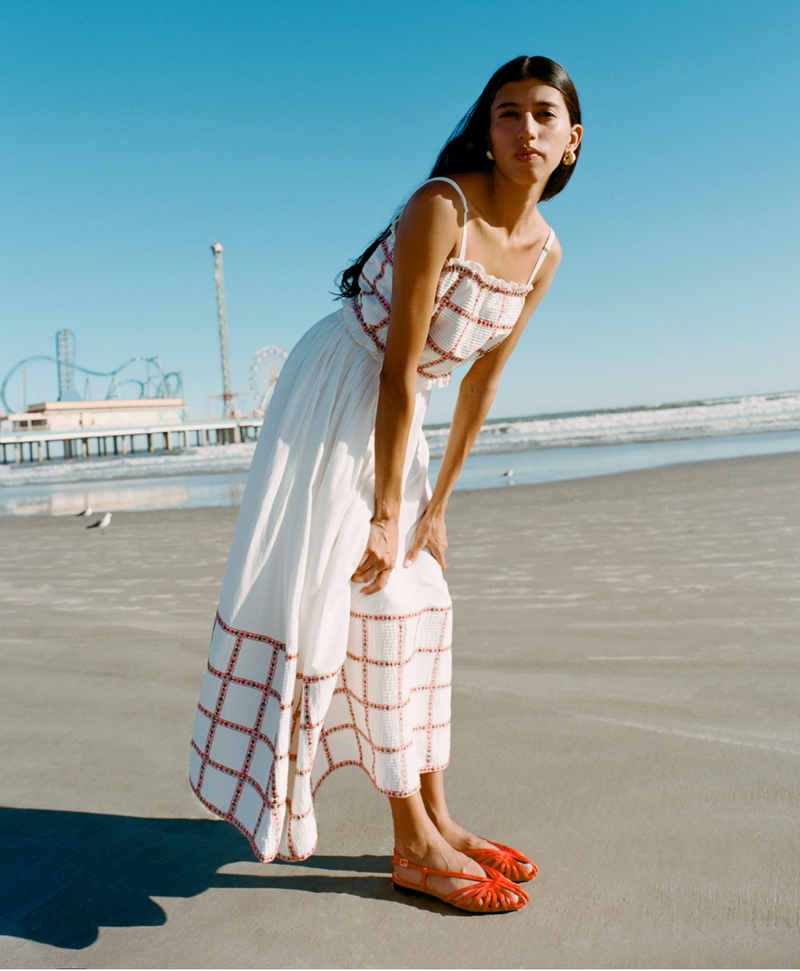 A model stands on the beach wearing a matching skirt and top set in white and red and strappy red flats.