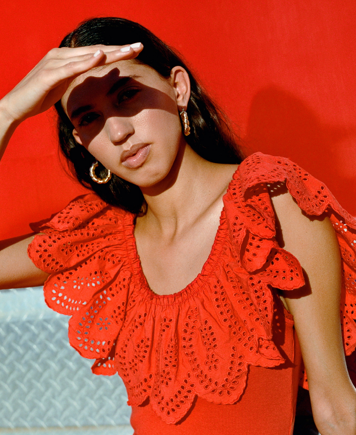 A model shades her eyes from the sun wearing a red eyelet top with details on the neck and shoulder.