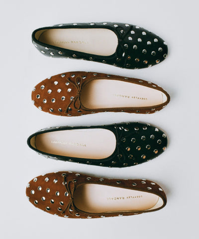 An overhead view of four studded flat sandals in black and brown on a light grey background.