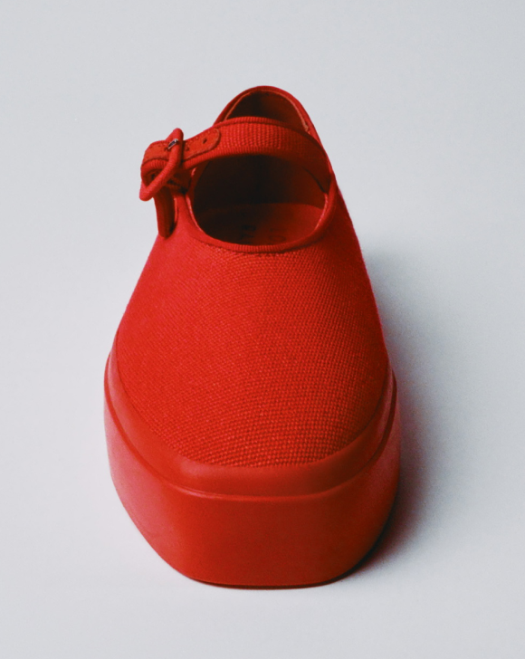 A close up of the front toe of a red mary jane sneaker on a grey background.
