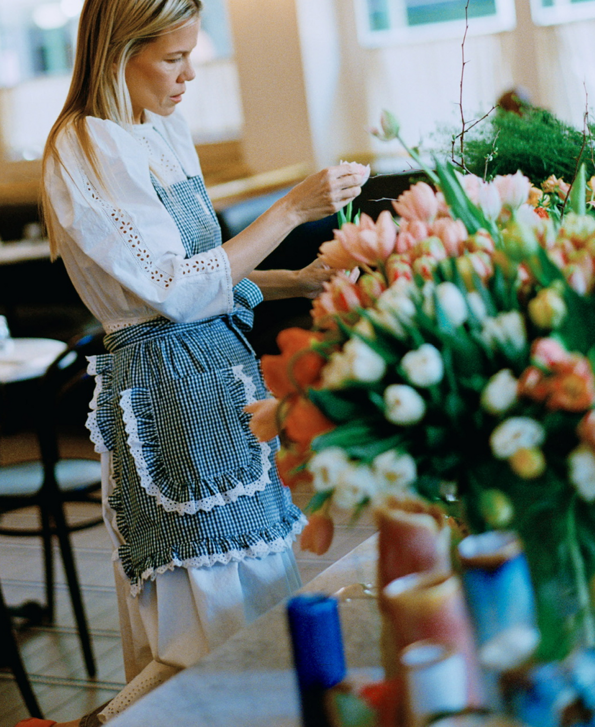 Jessie arranges a large bouquet of flowers while wearing a white eyelet dress and a green gingham apron.