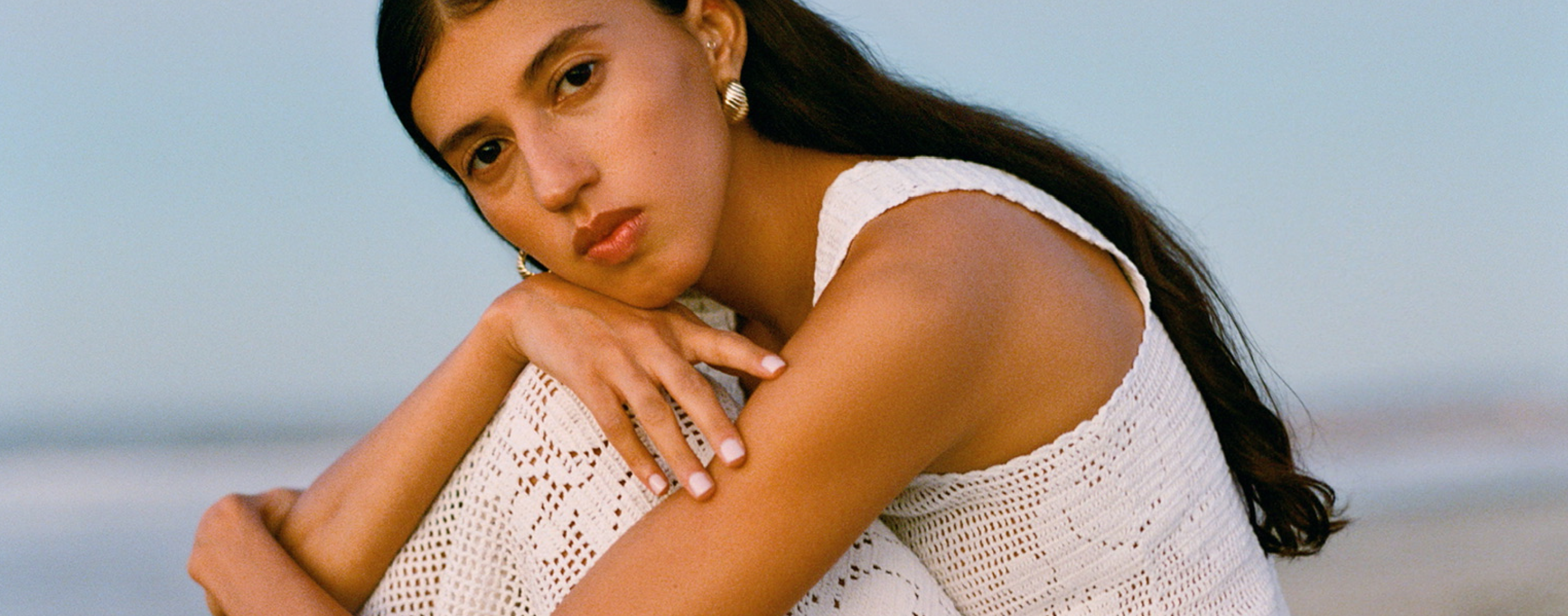A model wears a white crochet top and skirt set with gold earrings.