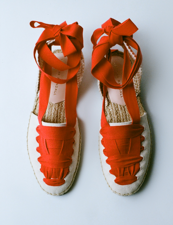 An overhead view of a pair of red lace up flat espadrilles on a grey background.