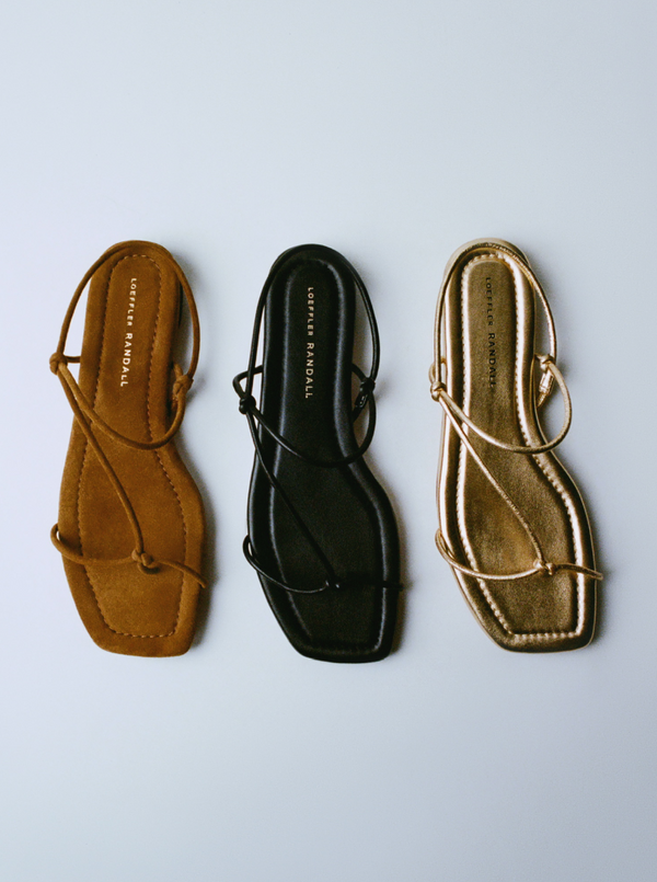 An overhead view of three strappy sandals in different colors on a grey background.