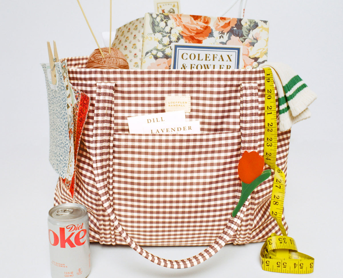 A side view of a brown gingham bag with items packed inside and in front on a white background.